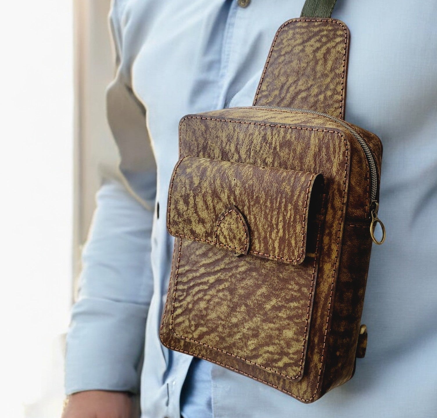Person wearing a brown leather crossbody bag with a light blue shirt.